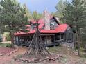 Log cabin with a red metal roof, stone chimney, and a cozy front porch featuring classic rocking chairs at 9716 Canon Dr, Sedalia, CO 80135