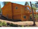 View of the home's back with wooden siding, showing a walkout basement, a small truck and lush trees at 10178 Hutch Ln, Conifer, CO 80433