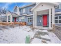 Blue townhome featuring a red front door, white trim, and a snowy yard with wooden fence at 6211 W 28Th Ct, Wheat Ridge, CO 80214