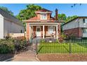 Charming red brick home with a cozy front porch, manicured lawn, and black wrought iron fence on a sunny day at 3016 N Franklin St, Denver, CO 80205