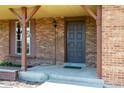 Close-up of a covered front porch with brick facade, wooden columns, and a dark-colored front door at 11098 Fairfax Way, Thornton, CO 80233