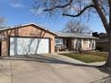Single-story home features a large two-car garage and is surrounded by a lush green lawn at 8757 W 75Th Way, Arvada, CO 80005