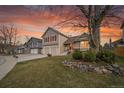 Two-story home with a lush front lawn, two car garage and striking red shutters, all under a beautiful sunset at 12028 W Aqueduct Dr, Littleton, CO 80127