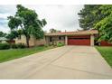 Charming brick home features a well-manicured lawn, mature trees, and a two-car garage with a red door at 1705 Lewis St, Lakewood, CO 80215
