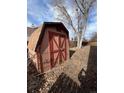 A rustic wooden shed with a red door, nestled amidst falling leaves and beneath the branches of a large tree at 11449 E 1St Ave, Aurora, CO 80010