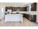 Modern kitchen with stainless steel appliances, island, and dark cabinets at 683 N Deer Park St, Watkins, CO 80137