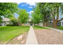 Inviting front yard with a well-maintained lawn and walkway leading to a charming home with mature trees at 1221 Ulster St, Denver, CO 80220