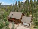 Aerial view of a two-story brown home with an attached garage surrounded by lush trees and partial mountain views at 32462 Lodgepole Dr, Evergreen, CO 80439