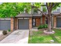 Inviting townhome featuring brick accents, a gray garage door, and a well-manicured lawn with a mature shade tree at 1953 E 102Nd Cir, Thornton, CO 80229