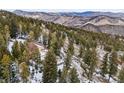 An aerial view of a home with mountain views, nestled in a wooded area on a snowy hillside at 1580 Santa Fe Mountain Rd, Evergreen, CO 80439