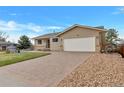Tan home featuring a paved driveway, two-car garage, and front lawn with river rock at 1882 S Zinnia Way, Lakewood, CO 80228