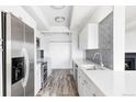 Galley kitchen with white cabinets, stainless appliances, light wood floors, and view to fireplace at 7877 E Mississippi Ave # 901, Denver, CO 80247