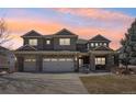 Inviting two-story home featuring a three car garage, brick accents, and colorful dusk sky at 8131 S Coolidge Way, Aurora, CO 80016