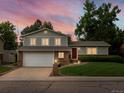 Two-story home at twilight with a red front door, attached two car garage, and a manicured front lawn at 13762 W 67Th Pl, Arvada, CO 80004