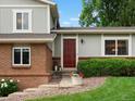 Close-up view of the red front door, brick facade, and landscaped garden in front of the two-story home at 13762 W 67Th Pl, Arvada, CO 80004