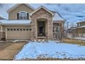 Inviting home featuring a stone-accented entrance, three car garage and snow-dusted winter yard at 14096 Roaring Fork Cir, Broomfield, CO 80023