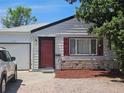 Close-up of a one-story home with a red door, contrasted by white siding and a stone foundation at 1233 Lansing St, Aurora, CO 80010
