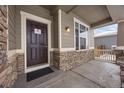 Inviting front porch with stone accents and a dark brown front door at 1523 Honeysuckle Ct, Brighton, CO 80601