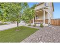 Charming home exterior with a welcoming porch, green lawn, stone accents, and mature landscaping at 56579 E 23Rd Pl, Strasburg, CO 80136