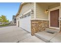 Close up of home exterior featuring a three-car garage with stone accents, and a covered front porch at 56579 E 23Rd Pl, Strasburg, CO 80136