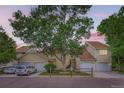 A sunset casts a glow over this tan townhouse with a two car garage and large shade tree at 461 S Kalispell Way # D, Aurora, CO 80017