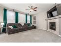 Comfortable living room featuring a plush gray sofa, fireplace, large windows with green curtains, and a ceiling fan at 10438 Olathe Way, Commerce City, CO 80022