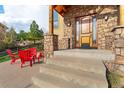 Inviting front porch with stone pillars, wooden door and trim, and comfortable red Adirondack chairs for relaxing in the Colorado sun at 3048 Starling Ct, Castle Rock, CO 80109
