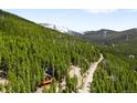 A tranquil mountain view with a quaint cabin surrounded by lush greenery and snow capped mountains in the distance at 489 Harris Dr, Idaho Springs, CO 80452