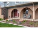 Inviting brick front porch with seating area, blossoming plants and a red front door at 6930 S Yukon Way, Littleton, CO 80128
