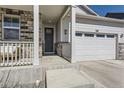 Inviting front porch with stone accents, leading to a home with an attached two-car garage and outdoor lighting at 45871 Orchid Ave, Bennett, CO 80102