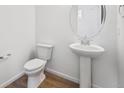 A half bathroom featuring a pedestal sink, toilet, and a round mirror, set against neutral walls at 6616 N Nepal St, Aurora, CO 80019