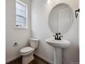 Modern half bathroom featuring a sleek pedestal sink, round mirror, and dark fixtures at 24708 E 40Th Ave, Aurora, CO 80019