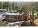 Inviting log cabin with a covered porch nestled among tall pine trees and snow at 27802 Shadow Mountain Dr, Conifer, CO 80433
