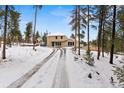 A serene home exterior on a snow-covered lot, framed by tall trees, with a long, inviting driveway at 27987 Pine Grove Trl, Conifer, CO 80433