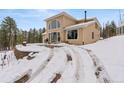 Two-story home featuring a large window and a patio, surrounded by snowy terrain and lush pine trees at 27987 Pine Grove Trl, Conifer, CO 80433