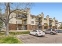 Multi-level condo building with balconies and brick accents, with a tree in the foreground at 481 S Kalispell Way # 205, Aurora, CO 80017