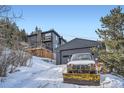 Exterior view of a mountain home and detached garage with a vehicle and snowplow parked outside at 11932 Coal Creek Heights Dr, Golden, CO 80403