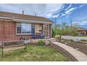 Close-up of a brick home's entry with seating, stone accents, and a tidy, landscaped yard at 3600 Olive St, Denver, CO 80207