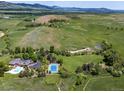 Expansive aerial view showcases a sprawling estate with tennis court, pool, and lush greenery against a mountain backdrop at 8000 N 41St St, Longmont, CO 80503