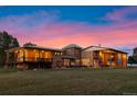 A panoramic exterior showcasing the home's architecture and spacious yard against a vibrant sunset at 11881 County Road 37, Fort Lupton, CO 80621