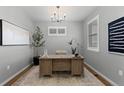 Home office showcasing a wooden desk, elegant chandelier, neutral walls, and ample natural light at 17969 Sky Pilot Ave, Parker, CO 80134