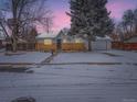 Charming single-story home with a brick facade, snow-covered yard, mature tree, and a whimsical treehouse at 469 S Routt Way, Lakewood, CO 80226