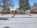 Charming single-story home with a brick facade, snow-covered yard, mature tree, and a whimsical treehouse at 469 S Routt Way, Lakewood, CO 80226