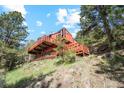 Exterior view of a rustic home with a sprawling wrap-around deck on a sloped lot surrounded by trees at 1278 Aspen Dr, Evergreen, CO 80439