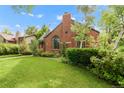 Lovely brick home with a chimney, arched windows, and vibrant green lawn and shrubs at 1226 Dexter St, Denver, CO 80220