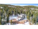 Aerial view of a gray mountain home nestled among tall pine trees with a snow-covered landscape and blue sky at 10747 Timothys Dr, Conifer, CO 80433