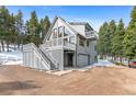 Gray mountain home with a deck, outdoor stairs, and attached garage surrounded by pine trees at 10747 Timothys Dr, Conifer, CO 80433