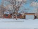 Charming single-story brick home with an attached garage and a snow-covered front yard in the winter at 1466 Elmwood Ln, Denver, CO 80221