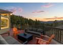 A wooden deck boasts outdoor seating with views of a lush forest and mountain range during sunset at 58 Stagecoach Blvd, Evergreen, CO 80439
