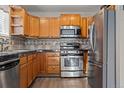 Well-lit kitchen with stainless steel appliances, wooden cabinets, and dark countertops at 3230 S Decatur St, Denver, CO 80236